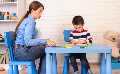 adhd-children-v1 Toddler boy in child occupational therapy session doing sensory playful exercises with her therapist.